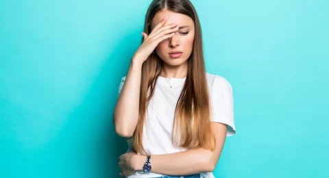 exhausted-woman-touching-head-while-standing-with-closed-eyes